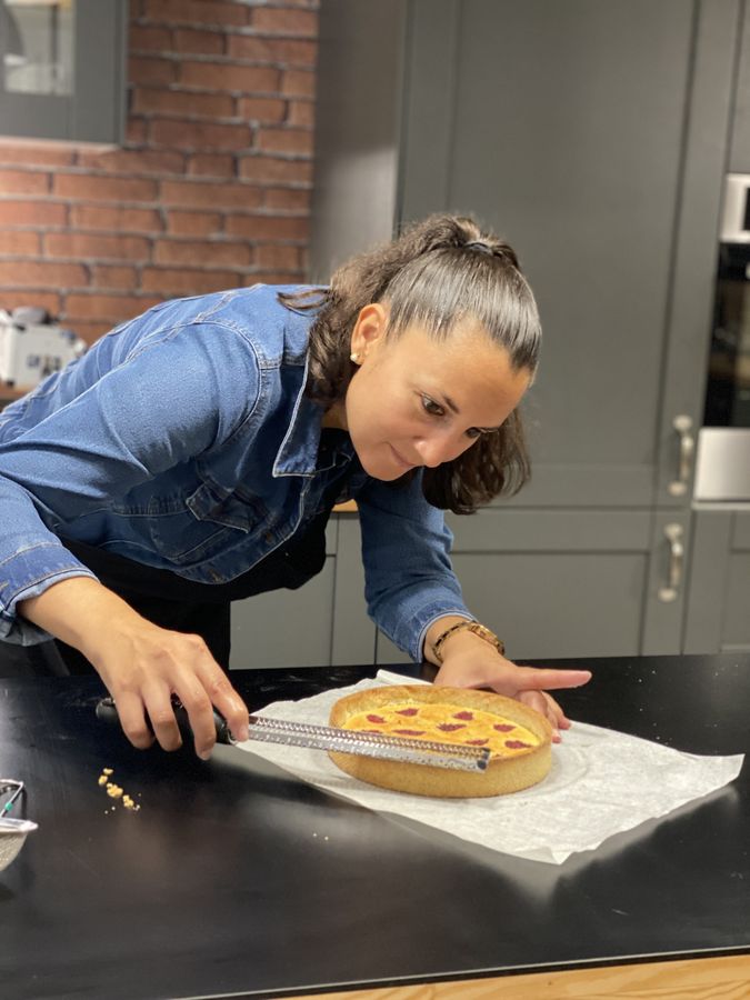 Participante souriante qui zeste le citron sur sa tarte aux framboises pendant un cours de pâtisserie privé