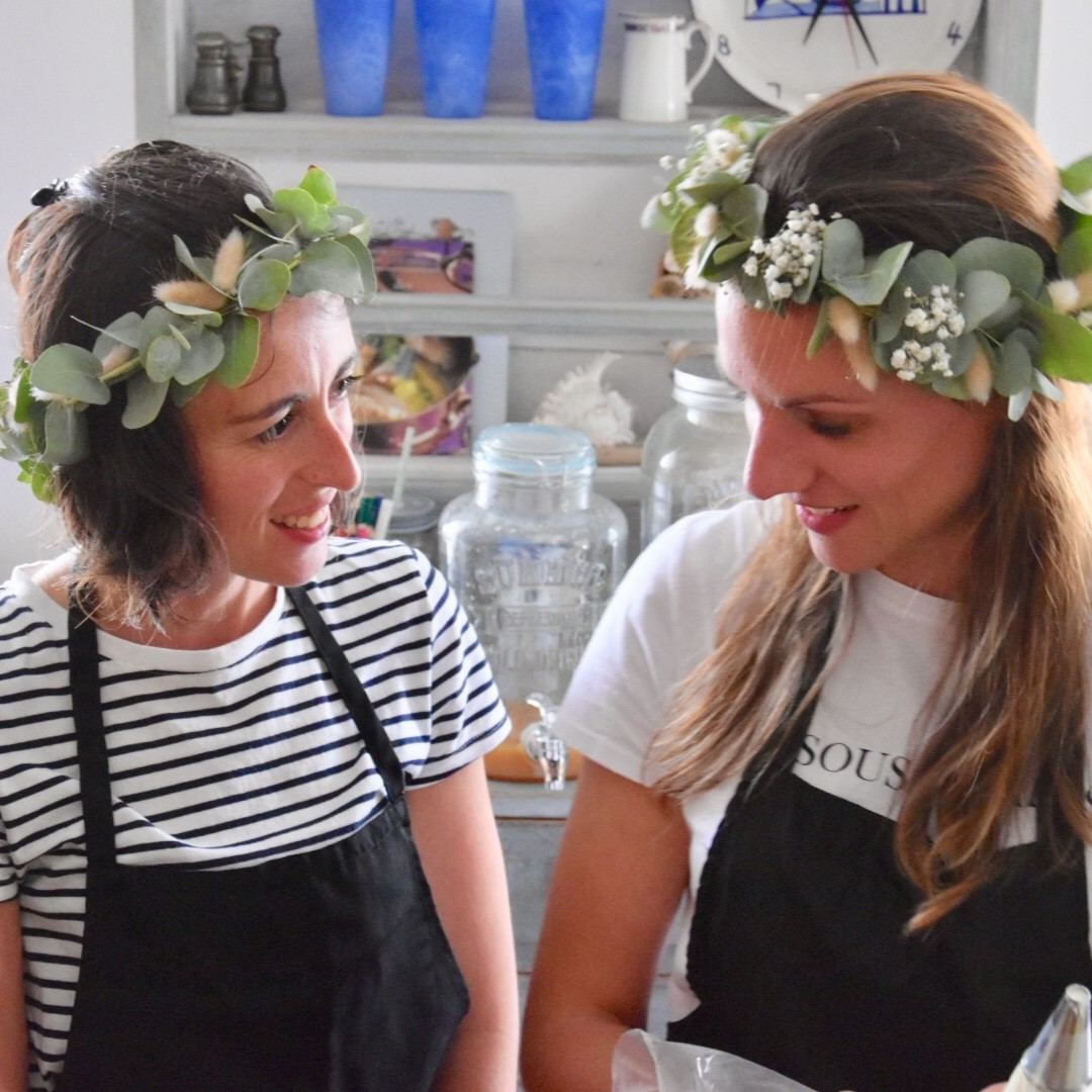 Future mariée et son amie en couronnes de fleurs pendant un atelier de pâtisserie pour un EVJF